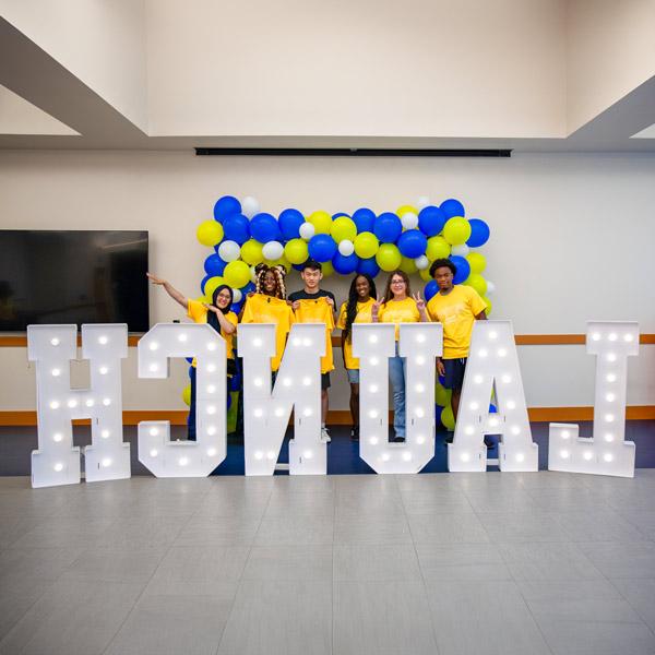 Students posing behind lighted letters that spell LAUNCH